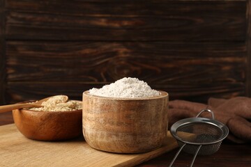 Brown rice, flour and sieve on wooden table. Space for text