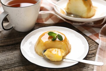 Delicious pudding with caramel sauce and mint served on wooden table, closeup