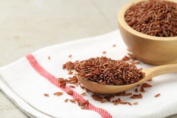 Brown rice in wooden spoon and bowl on table, closeup. Space for text
