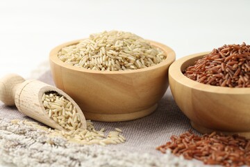 Different types of brown rice in bowls and scoop on table, closeup