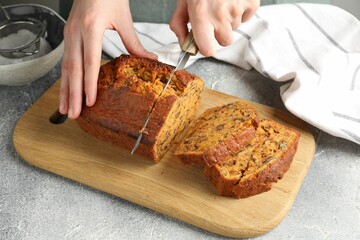 Woman cutting homemade carrot cake at grey table, closeup