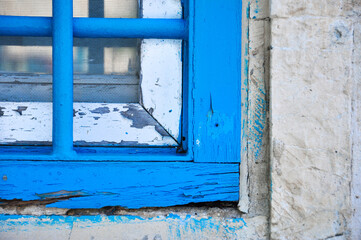 Charming rustic window frame painted in vibrant blue highlights charming decay and weathered textures against the neutral stone wall, fusing old-world charm with colorful artistry.