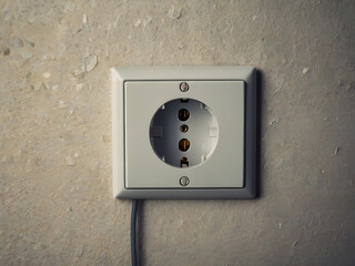 Power Socket: Close-up of a European power socket mounted on an aged, textured wall. The design presents a simple and functional aesthetic.