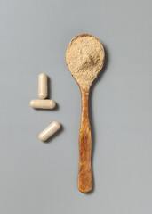 Medical capsules near wooden spoon full of beige powder on grey top view. Dietary supplements