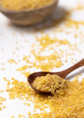 Raw dry uncooked yellow bulgur grain in a wooden spoon on white table cloesup. Ancient food