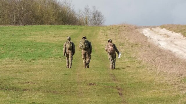 2 male and 1 female British army soldiers tabbing with 25Kg bergens across open countryside