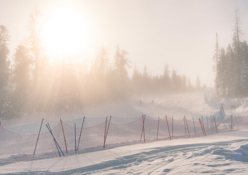 Sunlight filtering through fog on a snowy ski slope at a winter resort in the mountains during early morning hours