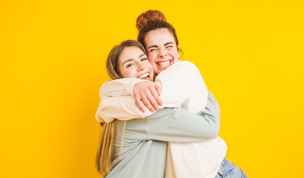 Two happy friends hugging and having fun on yellow background