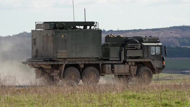 British army MAN SV HX 6x6 large dark green utility vehicle moving along a dirt track