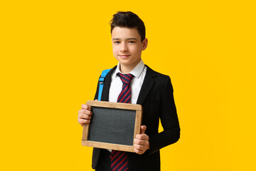 Cute schoolboy holding blank chalkboard on yellow background