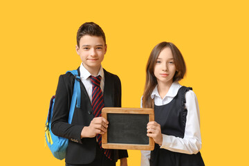 Schoolchildren holding blank chalkboard on yellow background
