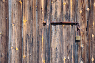 Close-up of a rustic wooden door with a metal latch and a secured padlock. Weathered wood texture and natural tones create a vintage look perfect for security, architecture, and countryside themes.