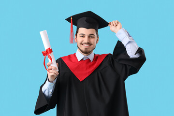 Cheerful male graduate student with diploma on blue background