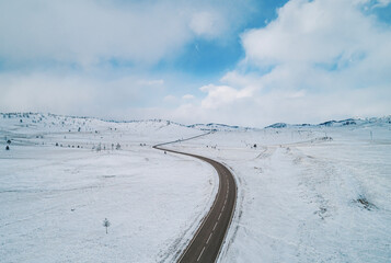 Snow-covered winding road through a winter landscape with blue sky in the background
