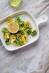 Serving tray with grilled Brussels sprouts on a grey granite background, vertical shot with space, view from above