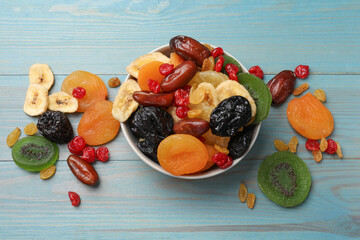 Mix of different dried fruits in bowl on light blue wooden table, flat lay