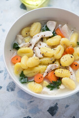 Bowl of chicken soup with potato gnocchi on a white and blue granite surface, vertical shot, middle close-up, selective focus