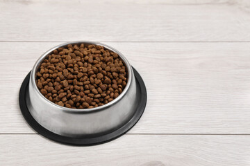 Dry pet food granules in feeding bowl on floor, space for text