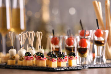 Many different tasty canapes on wooden table against blurred lights, closeup