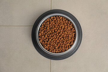 Dry pet food granules in feeding bowl on floor, top view