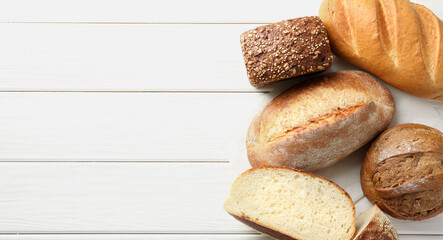 Whole and cut bread loafs on white wooden table, flat lay. Space for text