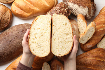 Woman with pieces of fresh bread over different other loafs at white table, top view