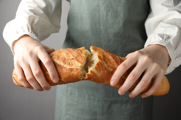 Woman breaking fresh baguette on grey background, closeup
