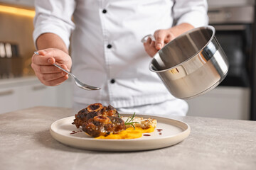 Professional chef adding sauce to delicious dish at table indoors, closeup