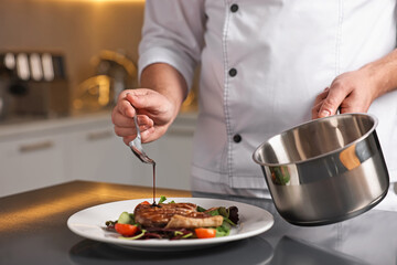 Professional chef adding sauce to delicious dish at table indoors, closeup