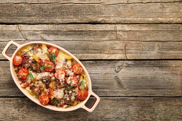 Delicious pasta casserole with cheese, tomatoes, minced meat and rosemary in baking dish on wooden table, top view. Space for text