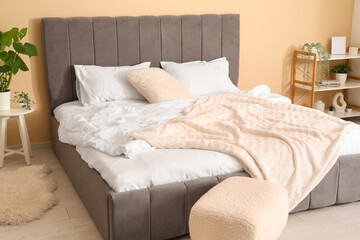 Comfortable bed, pouf and plant in bedroom
