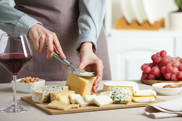 Woman slicing delicious cheese at light textured table indoors, closeup