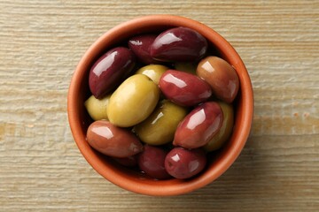 Tasty olives in bowl on wooden table, top view