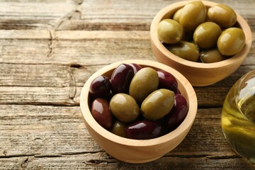Delicious marinated olives in bowls and oil on wooden table, closeup. Space for text