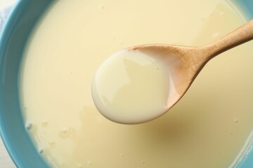 Taking tasty vanilla condensed milk with spoon from bowl on table, top view
