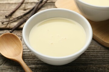 Tasty condensed milk, spoon and vanilla pods on wooden table, closeup