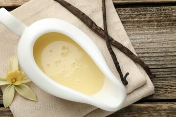 Tasty condensed milk, vanilla pods and flower on wooden table, flat lay