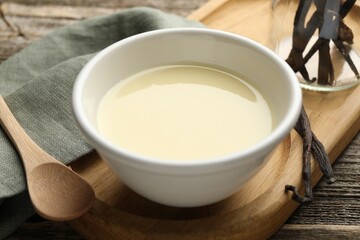 Tasty condensed milk, spoon and vanilla pods on wooden table, closeup