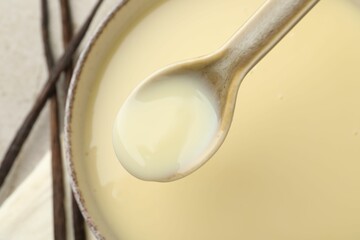 Taking tasty vanilla condensed milk with spoon from bowl on light grey table, flat lay