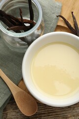 Tasty condensed milk, vanilla pods and spoon on wooden table, flat lay