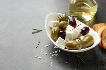 Marinated olives with feta cheese, bread pieces, oil, salt and rosemary on grey table, closeup. Space for text