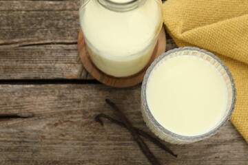 Delicious vanilla milk and pods on wooden table, flat lay. Space for text