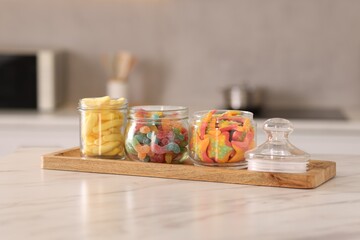 Tasty gummy candies in glass jars on white marble table