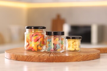 Tasty gummy candies in glass jars on white table