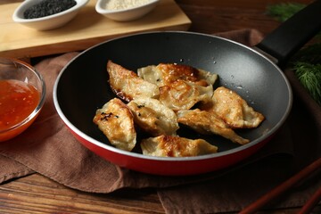 Tasty fried gyoza (dumplings) and sauce on wooden table, closeup