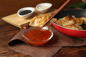 Dipping tasty fried gyoza (dumpling) into sauce on wooden table, closeup