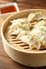 Tasty boiled gyoza (dumplings) in bamboo steamer on wooden table, closeup