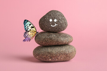 Happy stone glad to see butterfly, harmony. Stacked pebbles and one with smiling face on top against pink background