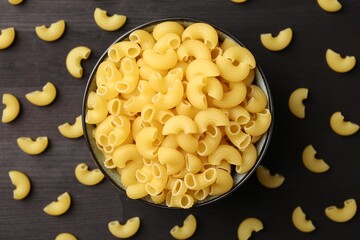 Raw horns pasta in bowl on dark wooden table, top view