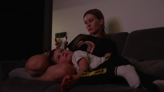 Sad baby with fever watches TV in mother's arms
